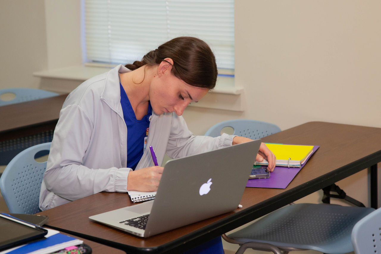 Student taking notes in classroom with laptop